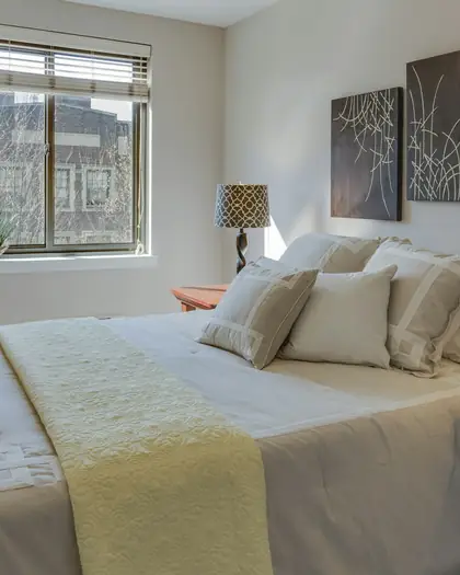 Made bed with cream pillows and a throw beside a sunny window