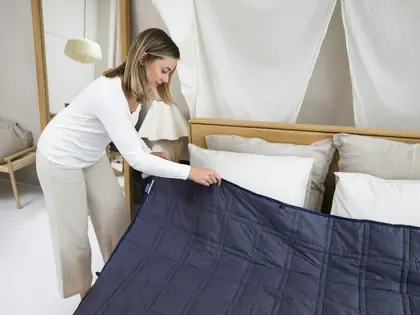 Woman spreading a navy blanket over a freshly made bed